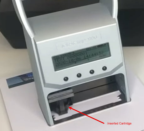 A close-up of a silver electronic testing device with a digital display screen and an open lower compartment showing an inserted cartridge, with a red arrow and text label pointing to it.